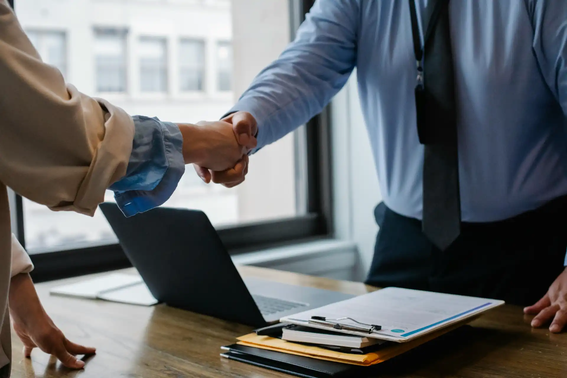 Business professionals shaking hands over a desk with a laptop, symbolizing expert support for heating solutions.