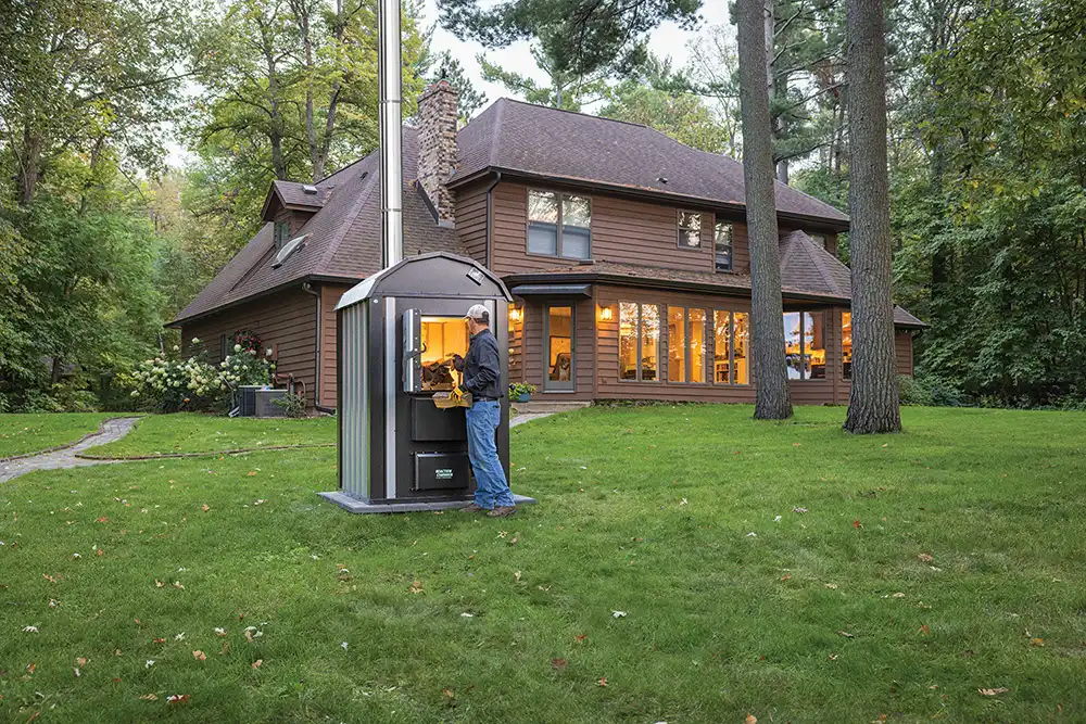 An outdoor wood boiler installed next to a house in the snow, ready for winter.